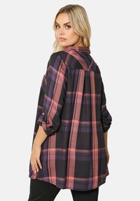 Camicia a quadri nera e rosa con maniche arrotolate, caratterizzata da una vestibilità ampia, dettagli con bottoni sulle maniche e un orlo posteriore più lungo.