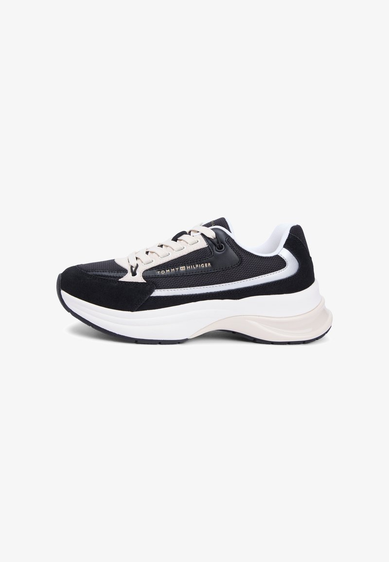 Fekete és bézs sportcipő strukturált felsőrésszel, velúr díszítésekkel, fehér középtalppal és oldalt díszítő logóval.