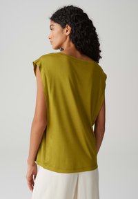 Top senza maniche di colore verde oliva, morbido e ampio, con una scollatura larga e un drappeggio delicato, realizzato in un tessuto morbido e liscio con una finitura pulita.