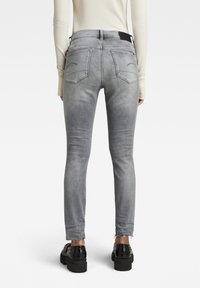 Jeans de mezclilla gris ajustados con un acabado desgastado, que presentan bolsillos traseros, una cinturilla con marca y detalles en el dobladillo deshilachado. Llevado con zapatos negros.