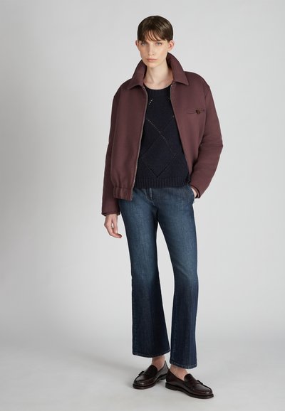 Chaqueta de cremallera color burdeos sobre un suéter de punto azul marino, combinada con jeans de campana azules y mocasines oscuros. Tejido suave con un diseño estructurado.