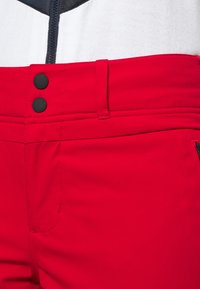 Rode broek met een gladde textuur, twee zwarte knopen in de taille en een ritszak aan de zijkant voor functionaliteit.