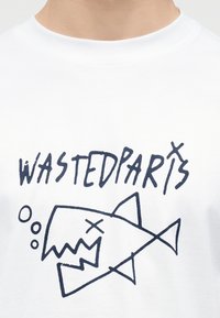 Λευκό μπλουζάκι με ένα γραφικό σε ναυτικό μπλε ενός στυλιζαρισμένου σκελετού ψαριού και το κείμενο "WASTED PARIS" από πάνω.