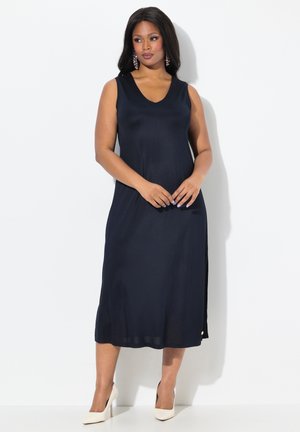 Navy ärmelloses Kleid mit V-Ausschnitt, Seitenriss und leicht dehnbarem Stoff. Kombiniert mit hellen, spitzen Absatzschuhen.