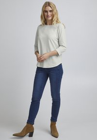 Hellgraues, gestreiftes Langarmoberteil mit abgerundetem Saum, kombiniert mit dunkelblauen Skinny Jeans und tanfarbenen Stiefeletten mit strukturiertem Absatz.