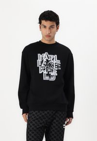 Svart sweatshirt med ett lager av vit och grå "KARL LAGERFELD" grafik, rund halsringning och ribbade ärmslut. Matcherade med mönstrade svarta byxor.