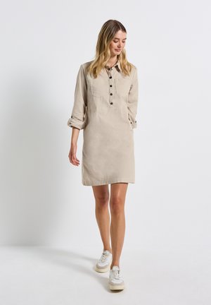 Ljusbeige skjortklänning med krage, knäppning framtill och två bröstfickor; designad i en avslappnad stil med uppvikta ärmar.