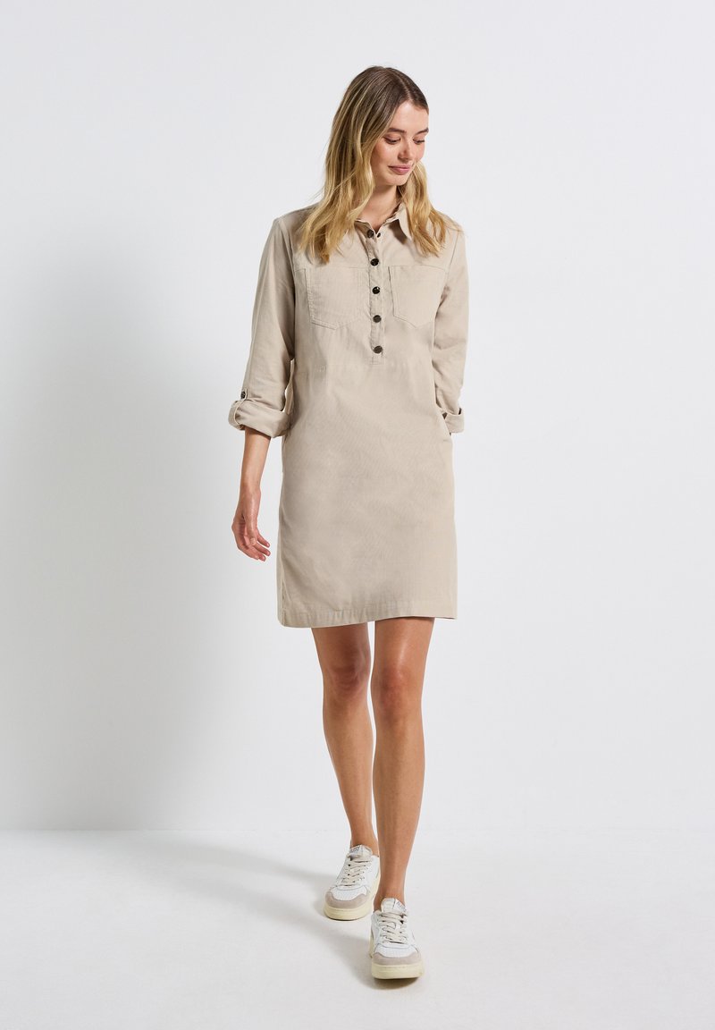 Robe chemise beige clair avec un col, une fermeture à boutons sur le devant et deux poches poitrine ; conçue dans un style décontracté avec des manches retroussées.