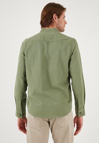 Chemise verte à manches longues en tissu texturé, avec des poignets boutonnés et un empiècement dans le dos. Dotée d'un ourlet arrondi et d'un col classique.