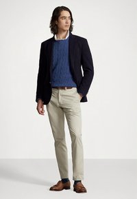 Granatowa marynarka, niebieski sweter w warkocze, beżowe chinosy, brązowe mokasyny. Gładkie tkaniny, dopasowany krój, jednolite kolory i klasyczne dodatki.