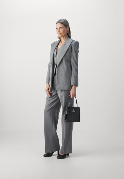 Pelēka pinstripe uzvalks ar pieguļošu žaketi un platām biksēm, kas apvienots ar melnu teksturētu rokassomu un melnajām papēžkurpēm. Gludi mati, minimāli aksesuāri.