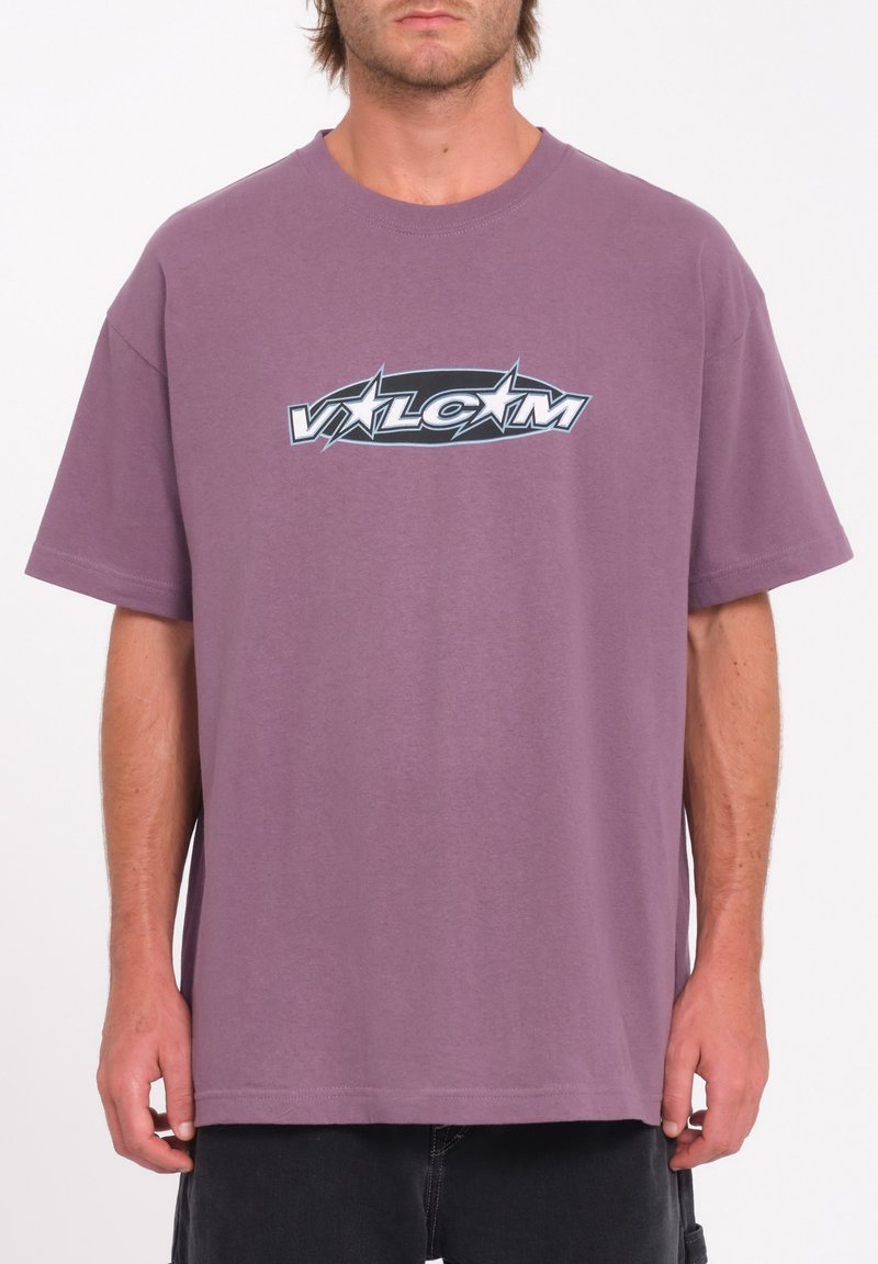 T-shirt en coton violet à manches courtes avec un design de logo graphique en noir et blanc sur le devant. Coupe décontractée, col rond.