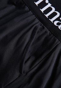 Primer plano de una tela negra con una banda elástica que muestra parcialmente texto en blanco y negro en la banda.