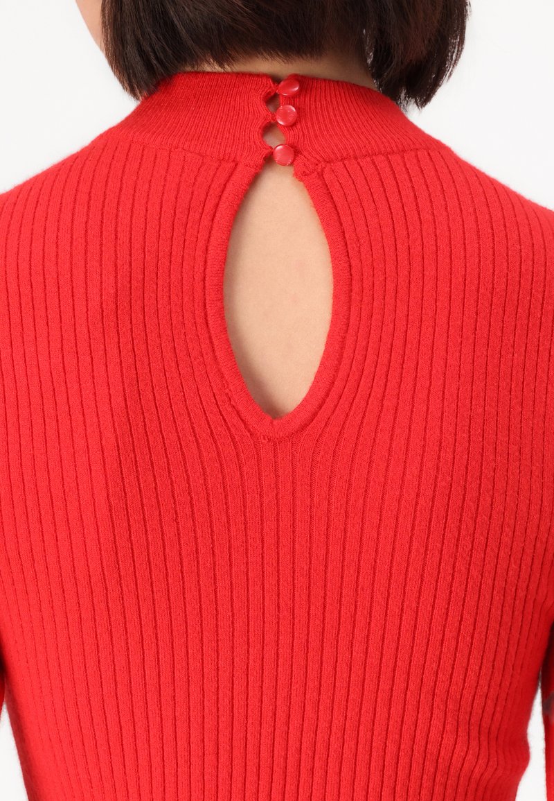 Czerwony sweter z prążkowanej tkaniny z wycięciem w kształcie klucza na plecach oraz trzema ozdobnymi guzikami. Tekstura jest gładka, a krój dopasowany.