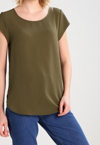 Haut vert olive à manches courtes avec un col rond, fabriqué en tissu léger, présentant une coupe décontractée et un ourlet légèrement arrondi.