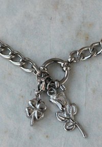 Braccialetto in argento con charm a forma di trifoglio e rosa. I charm sono dettagliati, con una consistenza liscia e una finitura lucida.