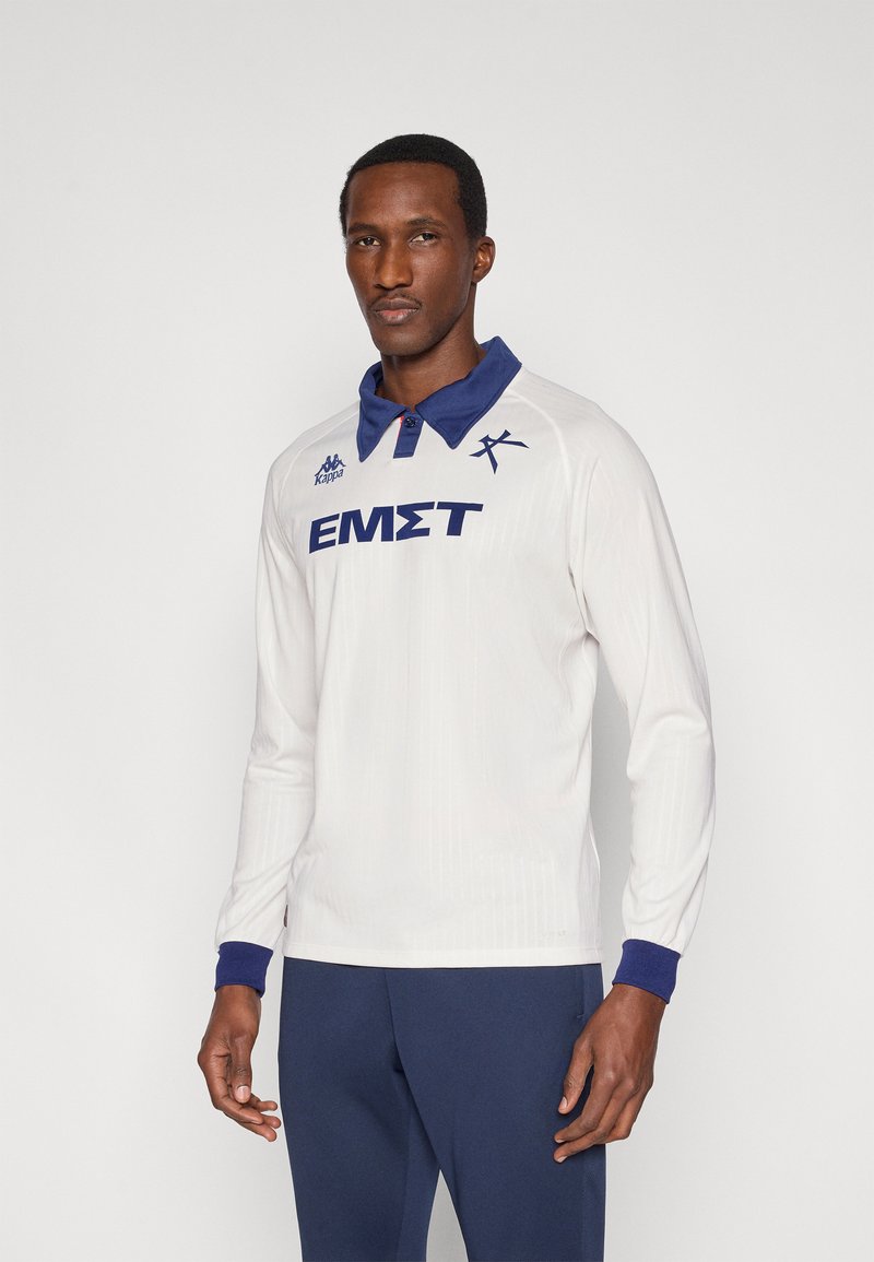 Baltas ilgomis rankovėmis polo marškinėlis mėlynu apykaklės ir rankogalio akcentu. Turi vertikalius ribinius raštus ir krūtinėje mėlynu užrašytą „ΕΜΣΤ“.