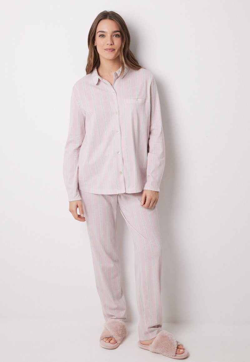 Completo pigiama in rosa chiaro e bianco a righe con accenti verdi. La camicia a maniche lunghe presenta una tasca sul petto. Abbinato a morbidi pantofole.