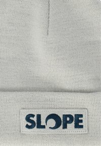 Ljusgrå mössa i stickad tyg. Har en nedvikt kant med en rektangulär etikett som visar ordet "SLOPE" i mörkblå bokstäver.