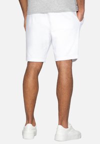Pantalones cortos de algodón blancos con bolsillos laterales, cinturilla elástica y un corte relajado. Combinados con zapatillas blancas.
