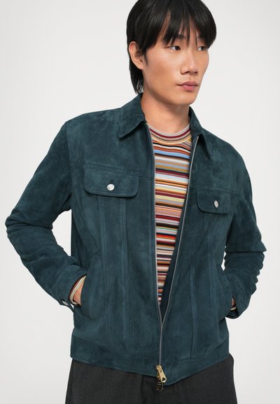 Veste en daim vert foncé avec fermeture éclair sur le devant, deux poches poitrine et un col pointu. Tissu texturé avec des détails de coutures verticales.