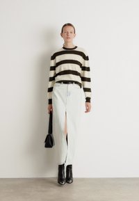 Randig stickad tröja i kräm och mörkbrunt, kombinerad med ljus denimkjol med slits framtill; modellen håller en liten svart väska och bär klackstövlar.