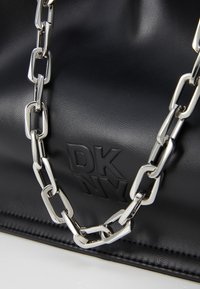 Juodas odinis rankinės dizainas su sidabriniu masyviu grandinės dirželiu ir iškilusiu "DKNY" logotipu. Tekstūruotas paviršius su įmantriu, moderniu dizainu.