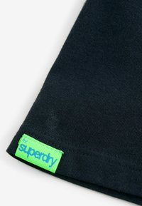 Tamno plavi pamučni majica s ovrtnicom i zelenom etiketom na kojoj piše "superdry", uz teksturiranu tkaninu i šivani rub.