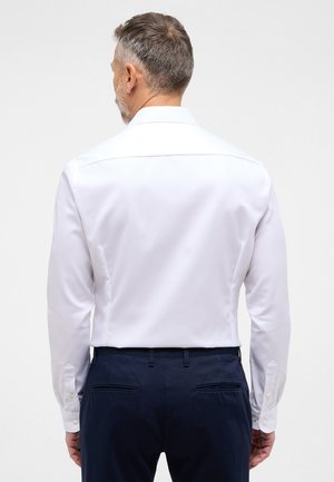 Weißes Langarmhemd mit strukturiertem Kragen, Knöpfen an den Manschetten, glatter Textur und taillierter Passform, getragen mit marineblauen Hosen.
