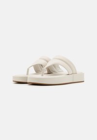 White flip-flop sandals with a smooth leather strap and a flat sole. The design features a minimalistic shape and subtle stitching details.