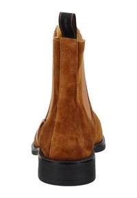 Stivali Chelsea in suede marrone con pannelli elastici laterali, suola in gomma nera e una linguetta con la scritta "GANT" sul retro. Texture liscia, design elegante.