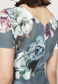 Robe à imprimé floral en tissu doux, dotée d'un dos en V, de manches courtes et d'un mélange de teintes vertes, roses et bleues avec des motifs de feuilles.