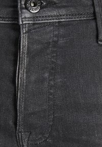 Tela de mezclilla negra con una textura suave, que presenta un cierre de botón, un bolsillo frontal y sutiles detalles de costura a lo largo de las costuras.