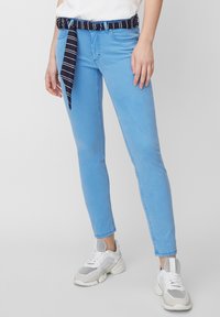 Vaqueros skinny de color azul claro con un cinturón de tela a rayas navy, que presenta una textura suave y un diseño de cinco bolsillos. Combinados con zapatillas blancas.