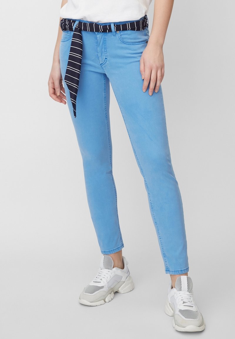 Vaqueros skinny de color azul claro con un cinturón de tela a rayas navy, que presenta una textura suave y un diseño de cinco bolsillos. Combinados con zapatillas blancas.