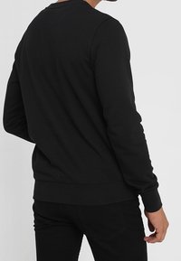 Černý pulovr s dlouhým rukávem a kulatým výstřihem, vyrobený z měkké látky, s přiléhavým pasem a manžetami, minimalistický design.