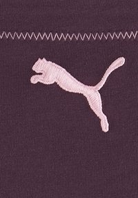 Lila Stoff mit pinkem, gesticktem Puma-Logo, das ein springendes Design zeigt und darüber zigzagförmige Nähte aufweist. Strukturiert Oberfläche.