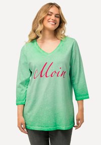 Grüner V-Ausschnitt-Tunika mit 3/4-Ärmeln, die ein Farbverlaufdesign zeigt, das von hellgrün zu dunkelgrün übergeht, und dem Wort "Moin" in pinker Schreibschrift.