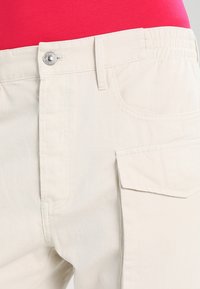 Ljust beige cargobyxor med elastisk midja, framknäppning med knapp och en sidoficka, tillverkade av ett slätt och slitstarkt bomullstyg.