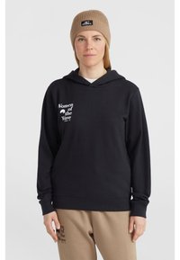 Black hooded sweatshirt with a white "Women of the Wave" print on the chest. Worn with beige sweatpants and a ribbed brown beanie.