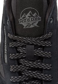 Svart mockaskor med texturerad ovandel, mörka snören och Reebok-logotyp. Har en vadderad krage och hållbar sömnad.