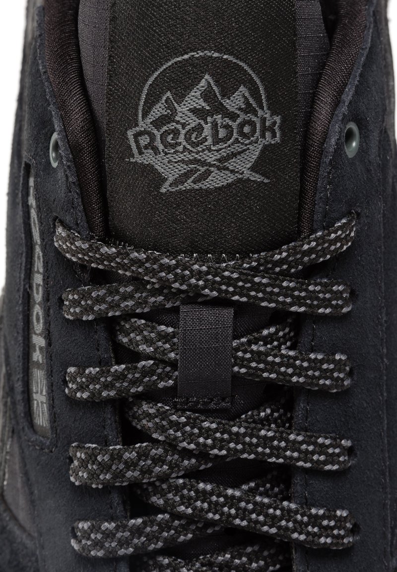 Czarne zamszowe sneakersy z teksturowaną cholewką, ciemnymi sznurówkami i logo Reebok. Posiadają wyściełany kołnierz i trwałe szwy.