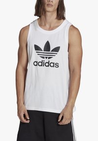 Balta medvilninė maikė su dideliu juodu Adidas logotipu ir trimis horizontaliomis juostelėmis viršuje. Dėvima kartu su juodomis šortais.