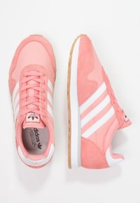 Rosa sneakers med vita ränder; ovandel som kombinerar mesh och mocka, sula av gummigummi och en rosa logotags på tungan.
