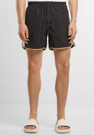 Shorts de bain noirs en tissu léger et texturé, avec une taille à cordon de serrage, des poches latérales et un liseré doré contrastant le long des jambes.