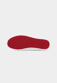 Semelle en caoutchouc rouge texturée d'une basket blanche avec le logo "Tommy Hilfiger" embossé sur la section du talon.