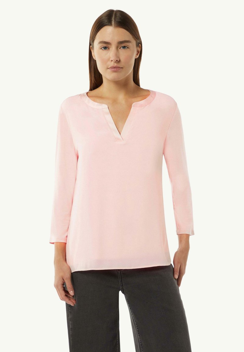 Light pink blouse with a V-neckline and three-quarter sleeves. Smooth texture and a relaxed fit, paired with dark jeans.