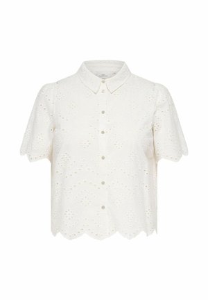 Blouse blanche à manches courtes avec boutons, broderie ajourée, ourlet festonné et col pointu, présentée sur un fond uni.
