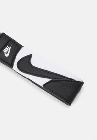 Zwart-wit leren polsband met een opvallend zwart Nike swoosh-logo, gestructureerd oppervlak en gladde randen.