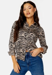 Camicia a maniche lunghe con bottoni in beige con strisce zebrate nere; realizzata in tessuto leggero con colletto e polsini arrotolati.